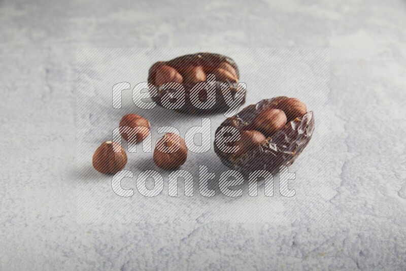 two hazelnuts stuffed madjoul dates on a light grey background