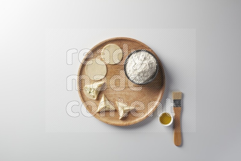 two closed sambosas and one open sambosa filled with cheese while flour, and oil with oil brush aside in a wooden dish on a white background