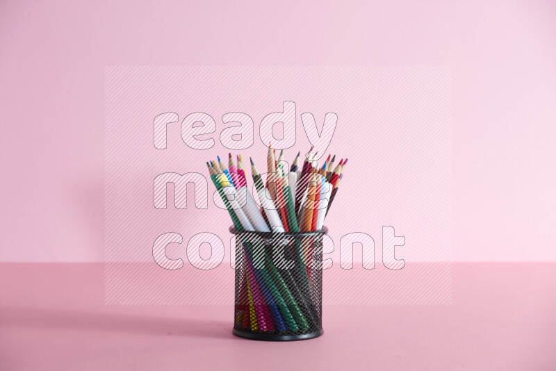Pens, pencils and other different school supplies in a metal pen holder on rose background