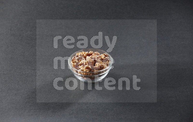 A glass bowl full of peeled walnuts on a black background in different angles