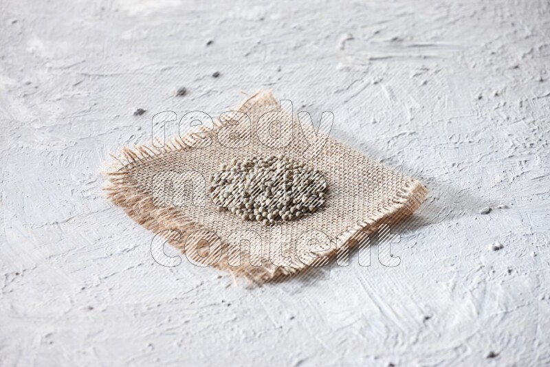 White pepper beads on a burlap piece of fabric on textured white flooring