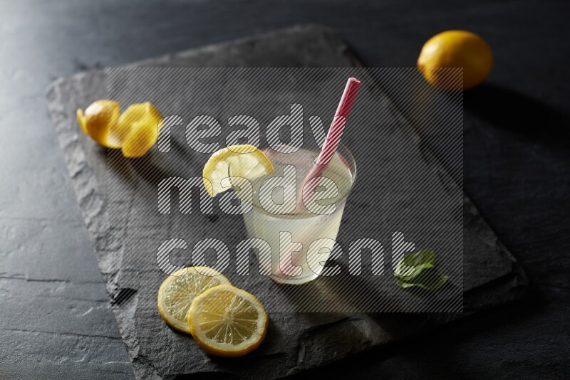 A glass of lemon juice with a straw on black background