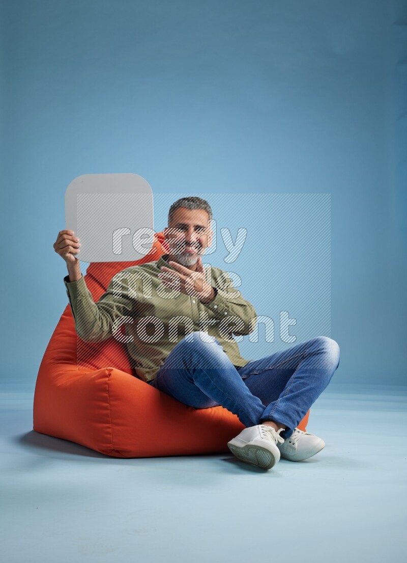 A man sitting on a orange beanbag and holding social media sign