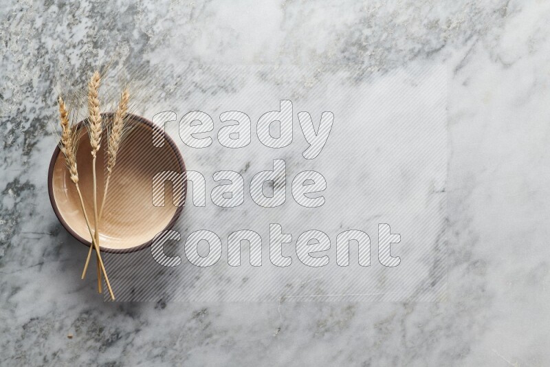 Wheat stalks on beige pottery oven bowl on grey marble background