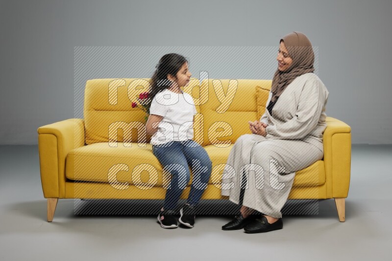 A girl sitting hiding flowers behind her back for her mother on gray background