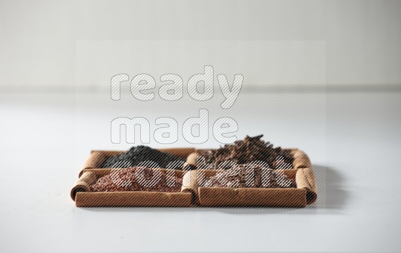 4 squares of cinnamon sticks full of black seeds, cloves, flaxseeds and garden cress on white flooring