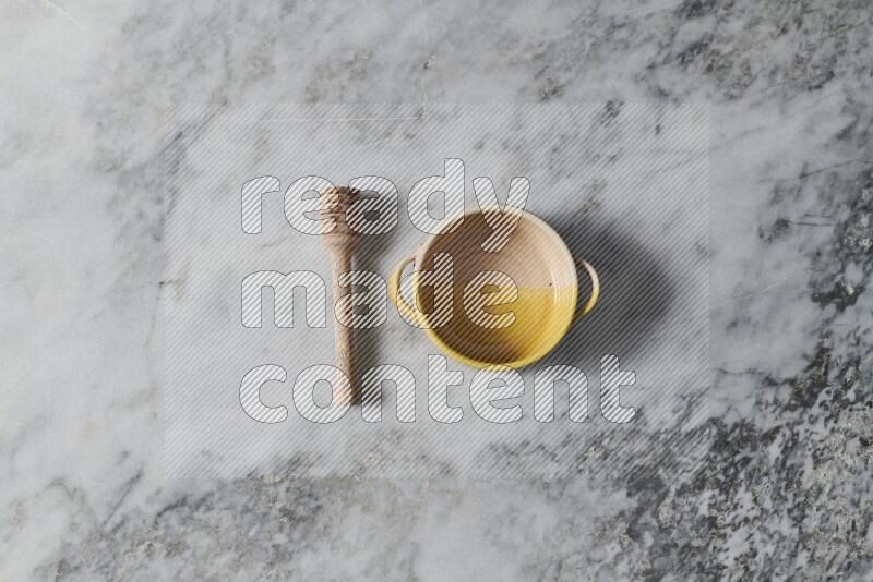 Multicolored pottery bowl with wooden honey dipper on the side on grey marble background