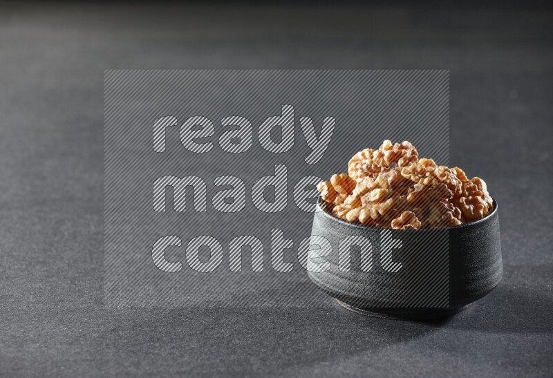 A black pottery bowl full of peeled walnuts on a black background in different angles