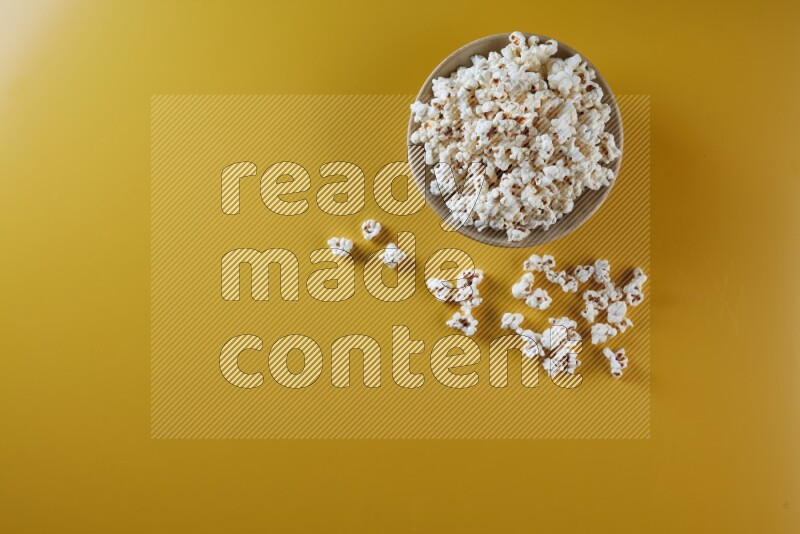A multicolored ceramic plate full of popcorn with popcorn beside it on a yellow background in different angles