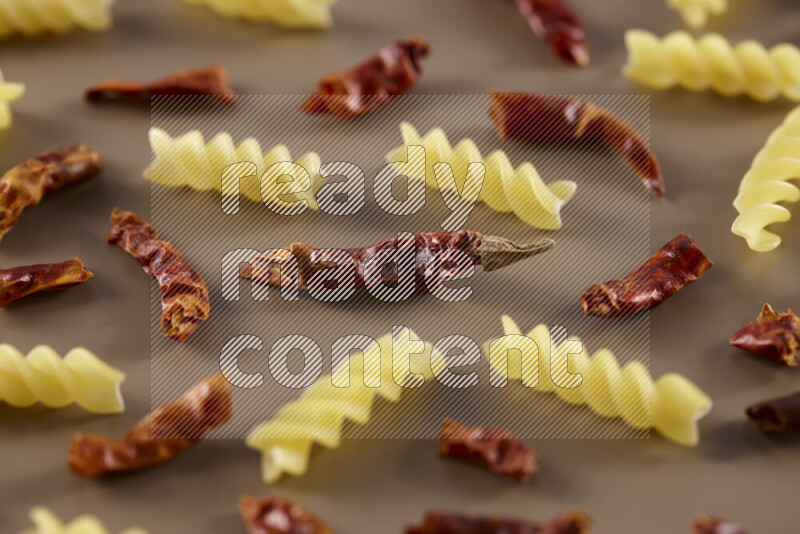 Raw pasta with different ingredients such as cherry tomatoes, garlic, onions, red chilis, black pepper, white pepper, bay laurel leaves, rosemary and cardamom on beige background