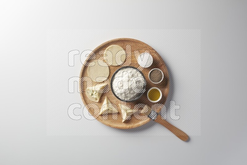 two closed sambosas and one open sambosa filled with cheese while flour, salt, black pepper and oil with oil brush aside in a wooden dish on a white background