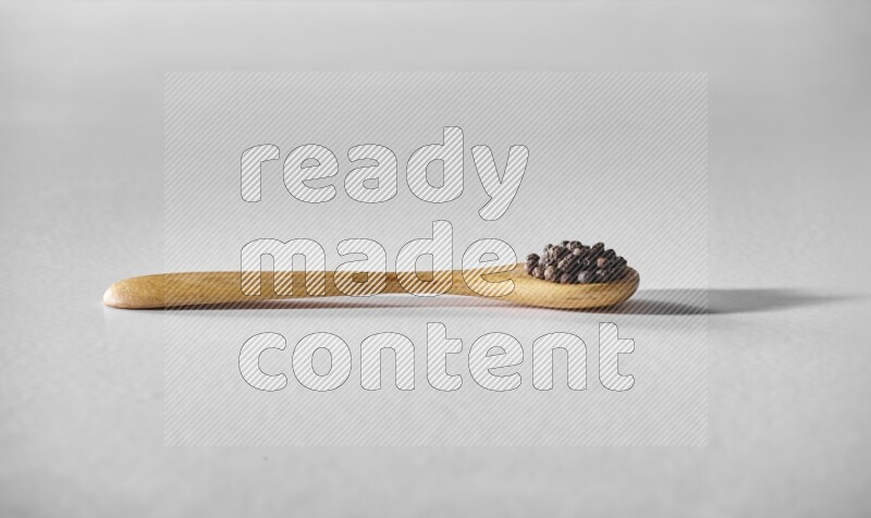 A wooden spoon full of black pepper on white flooring