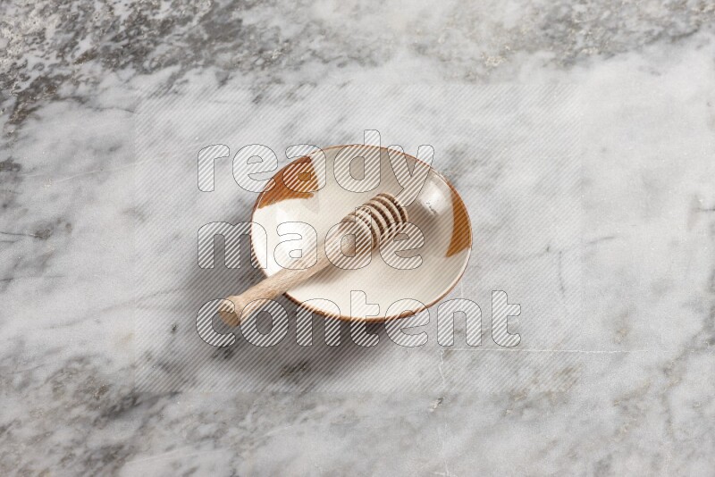 Multicolored pottery plate with wooden honey dipper in it on grey marble background