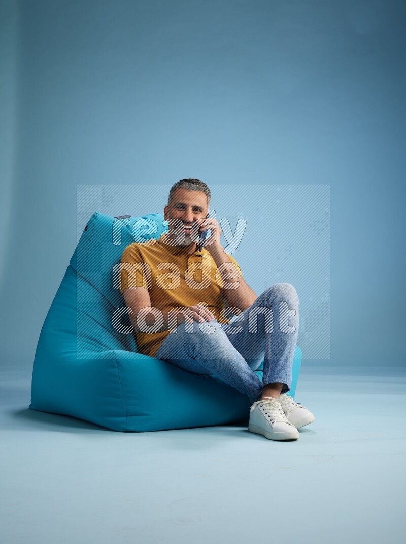 A man sitting on a blue beanbag and talking on the phone