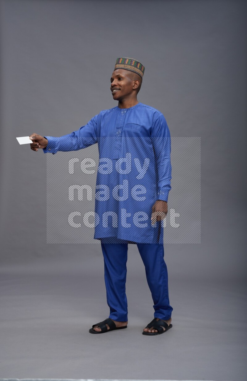 Man wearing Nigerian outfit standing holding ATM card on gray background
