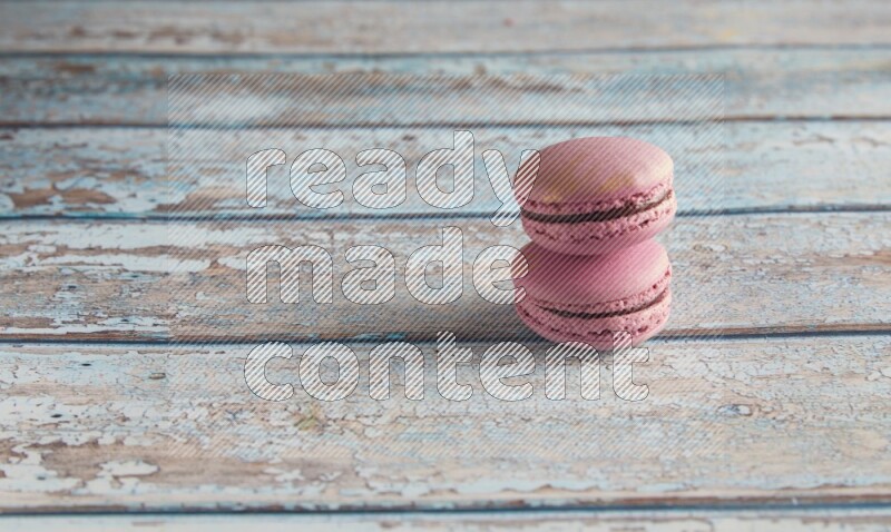 45º Shot of two Purple Strawberry macarons on light blue wooden background