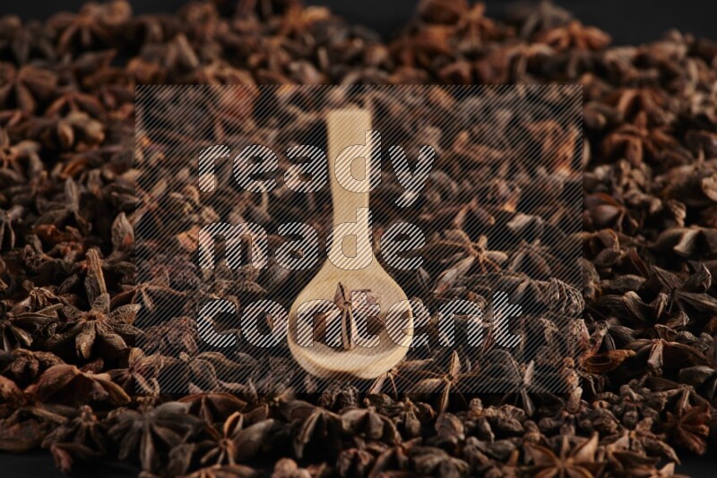 Star Anise in a wooden spoon on more stars anise filling the frame on black flooring