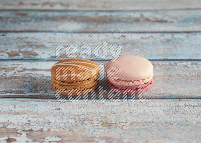 45º Shot of of two assorted Brown Irish Cream, and Pink Litchi Raspberry macarons on light blue background