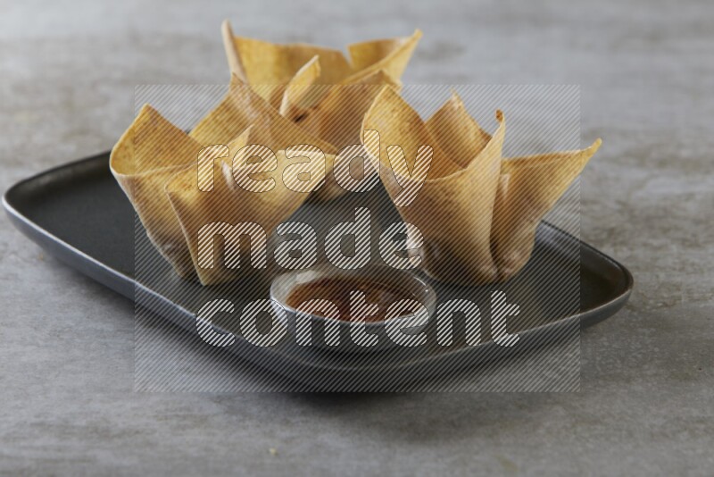 wonton cups with soy sauce ramkin on rectangle dark grey ceramic plate on grey textured counter top