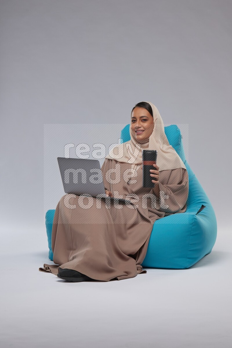 A Saudi woman sitting on a blue beanbag and working on laptop