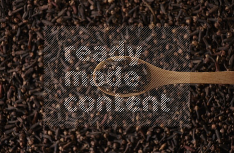 A wooden spoon full of cloves on cloves background and black flooring