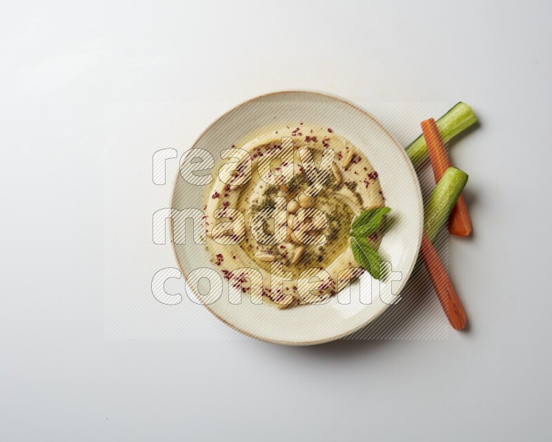 Hummus in a pottry plate garnished with zaatr & sumak on a white background