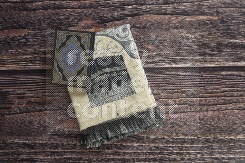 A folded prayer mat with different elements such as quran and prayer beads on brown wooden background