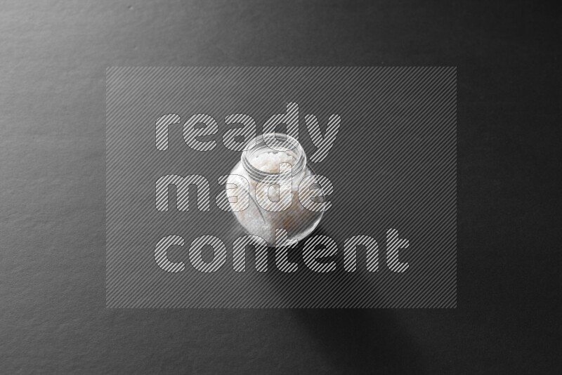 A glass spice jar full of salt on black flooring