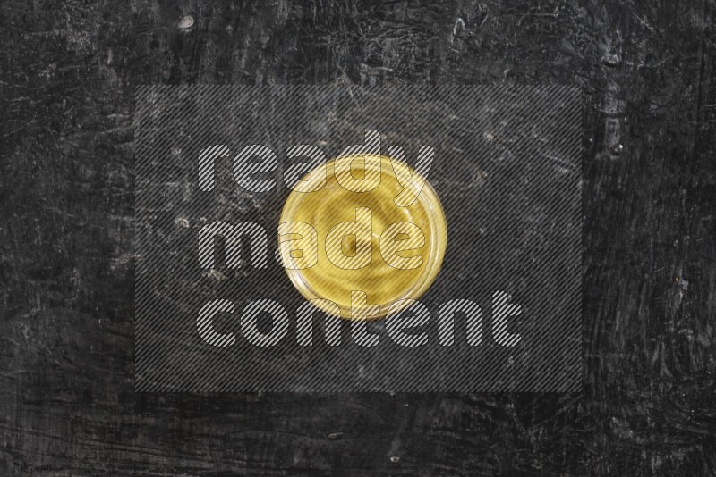 A glass jar full of mustard paste on a textured black flooring