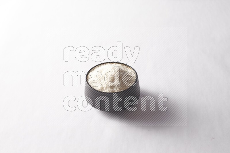 Desiccated coconuts in a black pottery bowl on white background