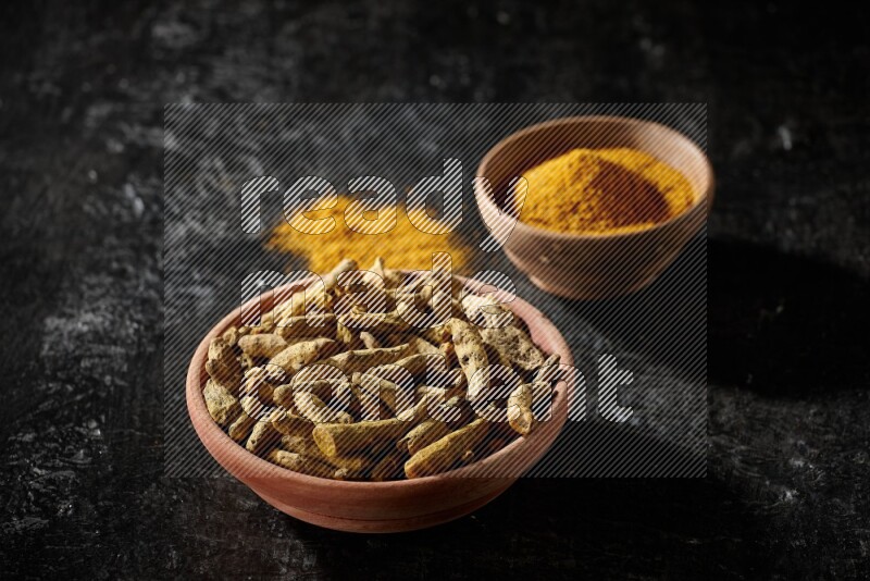 وعاءان خشبيان، أحدهما ممتلئ ببودرة الكركم والآخر بأصابع الكركم المجففة، على خلفية سوداء