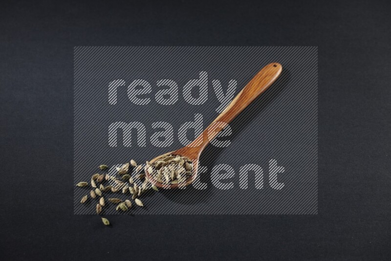 مغرفة خشبية ممتلئة بالهيل على خلفية سوداء