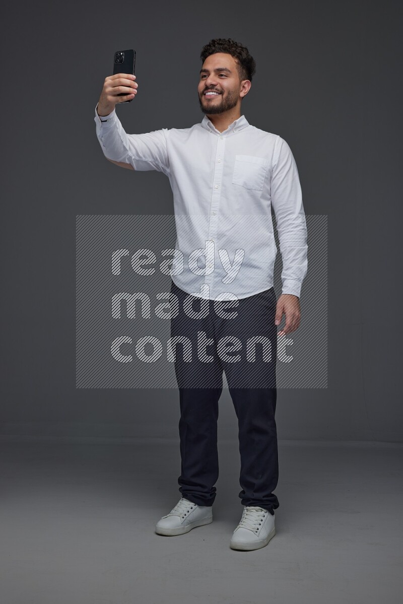 A man wearing smart casual and taking selfie with his phone eye level on a gray background