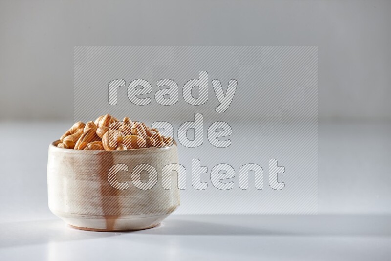 A beige ceramic bowl full of cashews on a white background in different angles