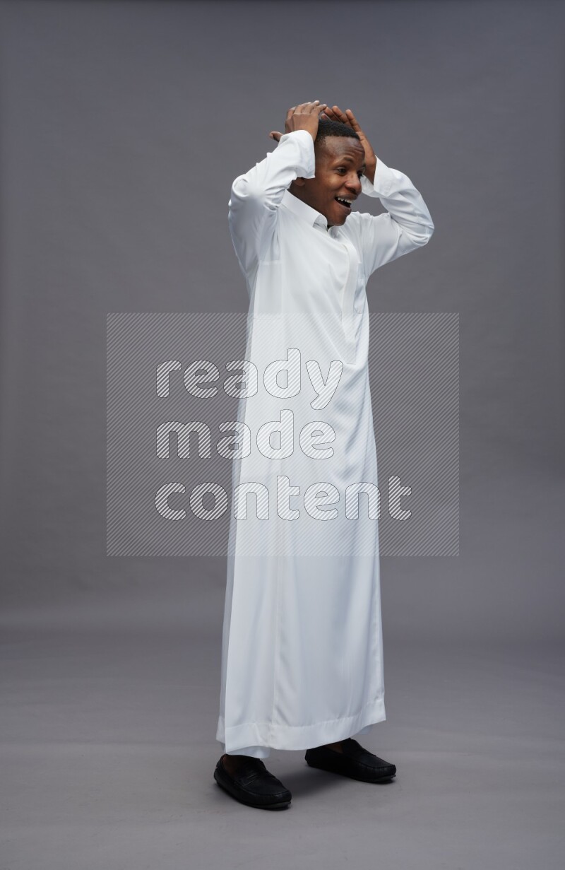 Saudi man wearing thob standing hands behind head on gray background