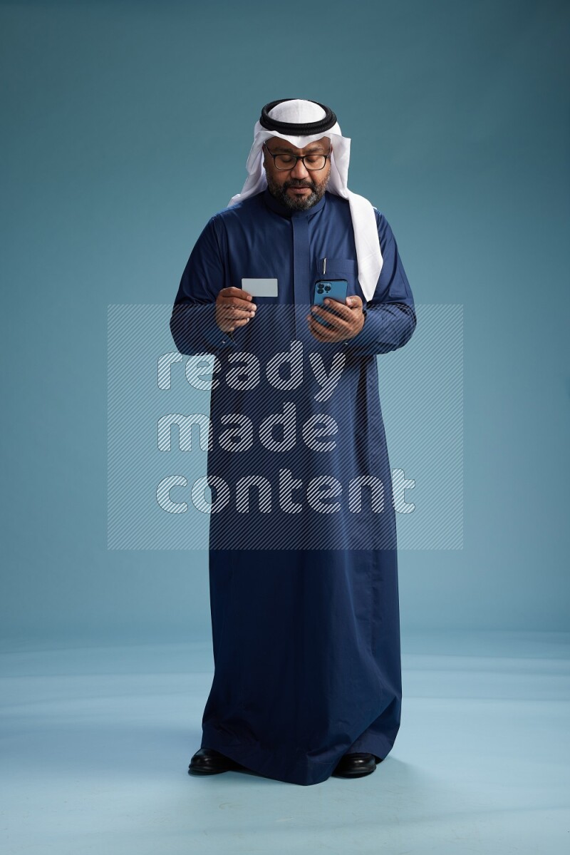 Saudi Man with shimag Standing holding ATM card while talking on phone on blue background