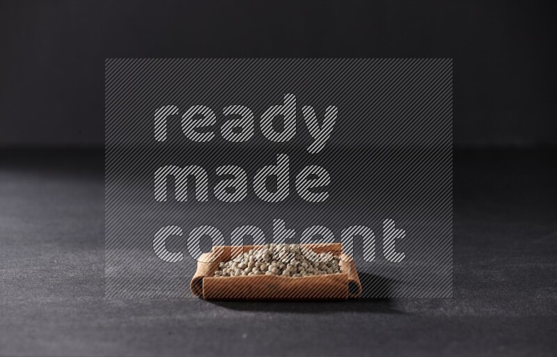 أربعة من أعواد القرفة مكونة شكل مربع بداخلها حبوب الفلفل الأبيض علي خلفية سوداء