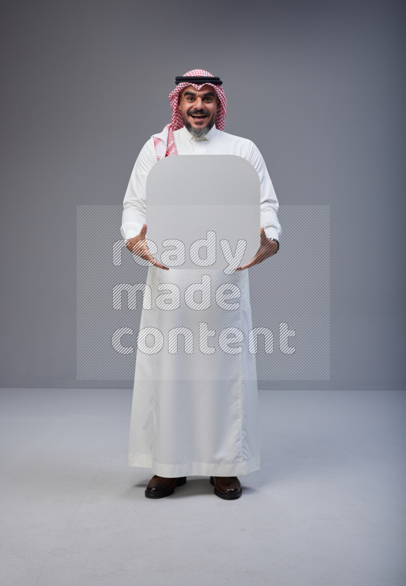 Saudi man Wearing Thob and red Shomag standing holding social media sign on Gray background