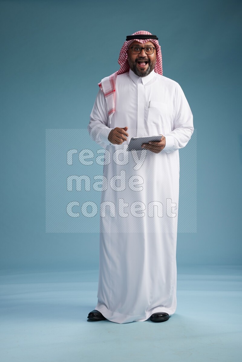 Saudi Man with shimag Standing holding a tablet on blue background