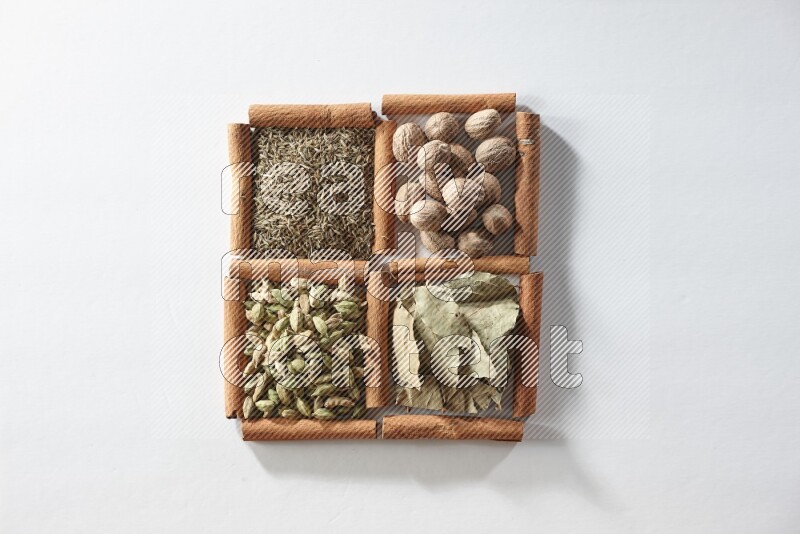 4 مربعات من أعواد القرفة ممتلئة بجوزة الطيب وأوراق الغار وحبوب الهيل والكمون على أرضية بيضاء