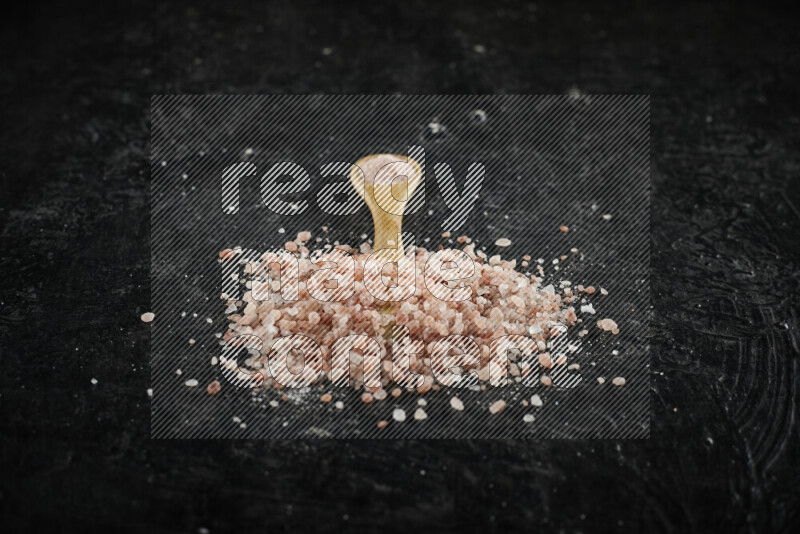 A wooden spoon full of pink himalayan salt on black background