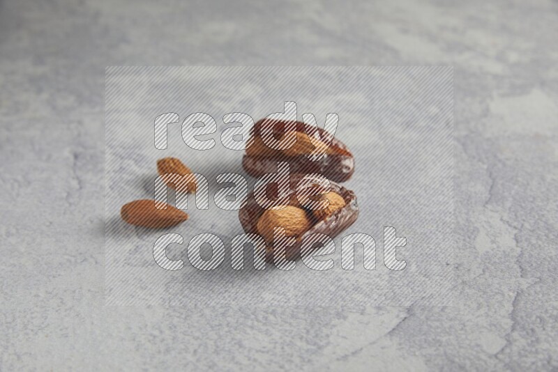 two Almond stuffed date with unroasted  almonds on a light grey background