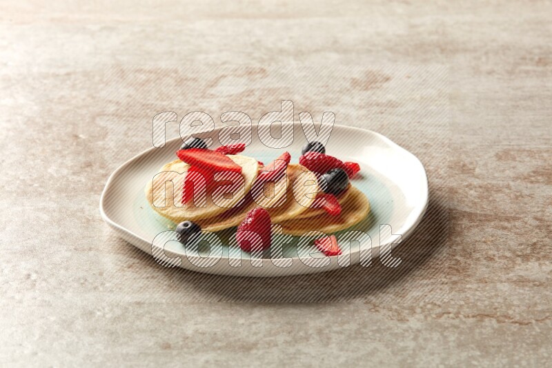 Five stacked mixed berries mini pancakes in a bicolor plate on beige background
