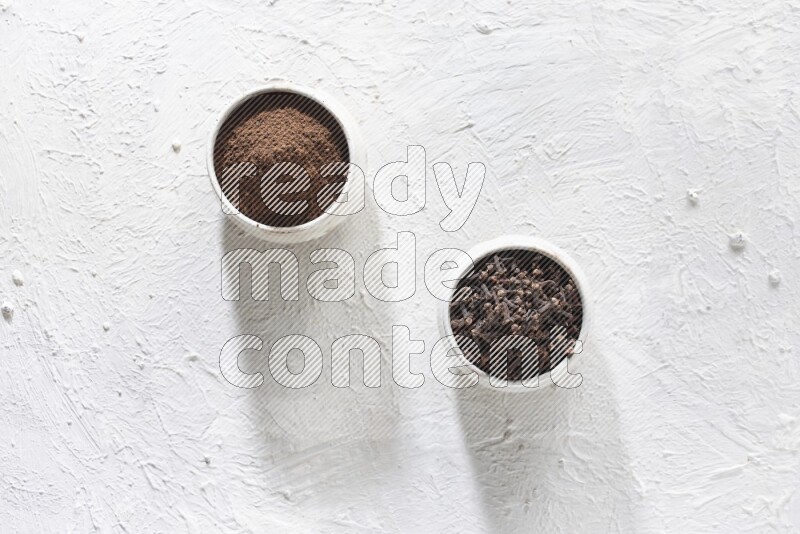 2 Beige ceramic bowls, one full of cloves and the other full of powder on textured white flooring
