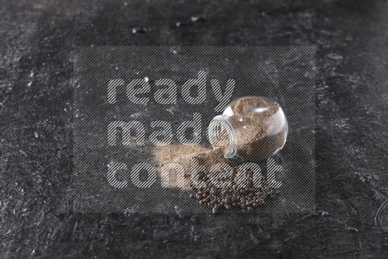 بودرة الفلفل الأسود في وعاء زجاجي مقلوب مع حبوب الفلفل الأسود بجانبه علي خلفية سوداء