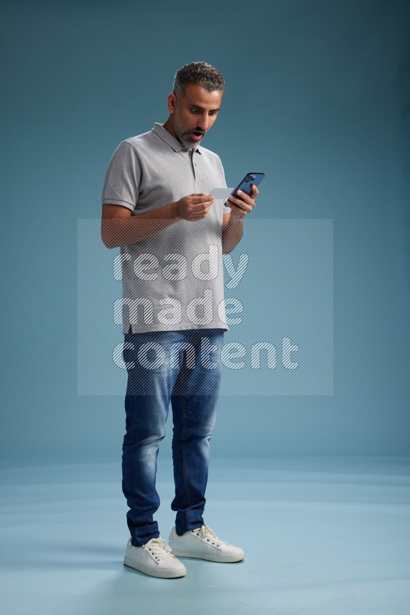 Man Standing holding ATM while talking on phone on blue background