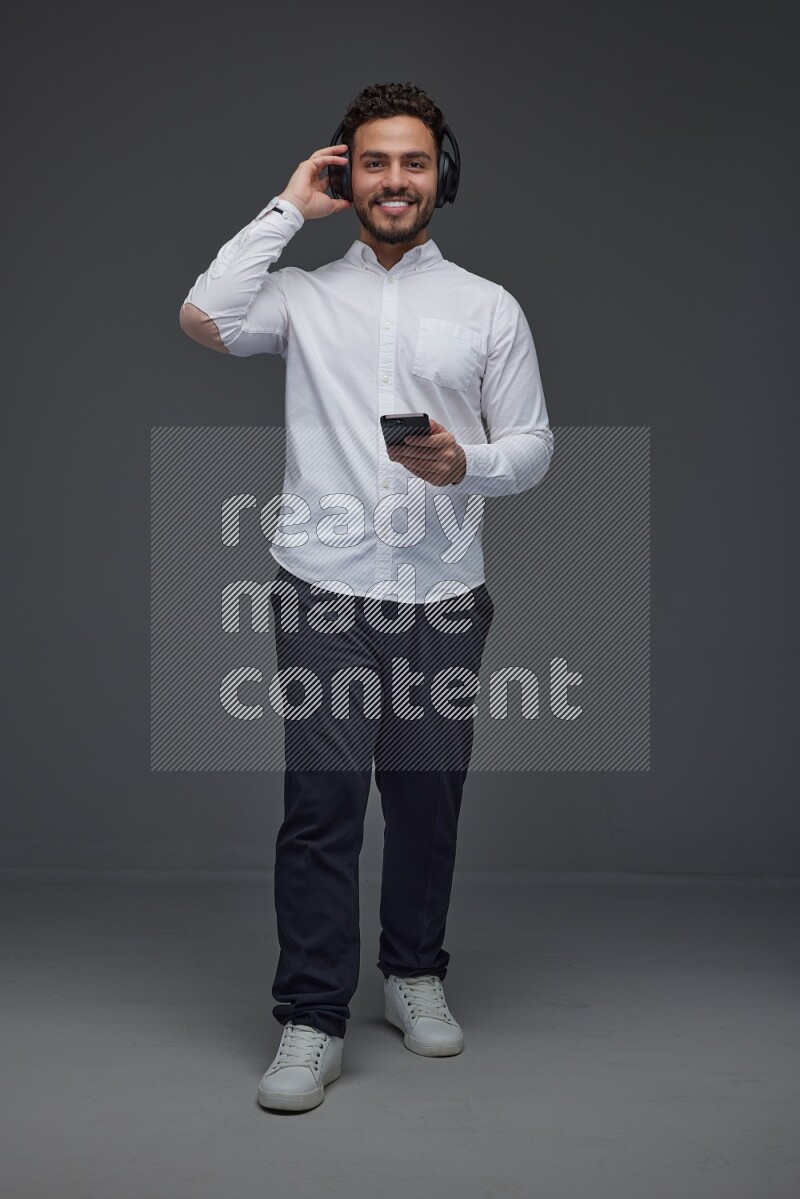 A man wearing smart casual and using his phone and headphone eye level on a gray background