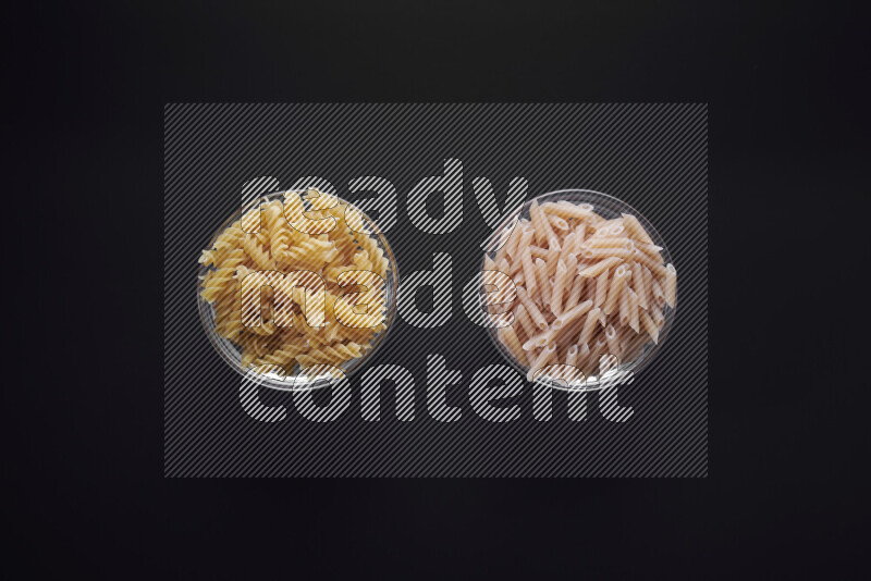 Different pasta types in glass bowls on black background