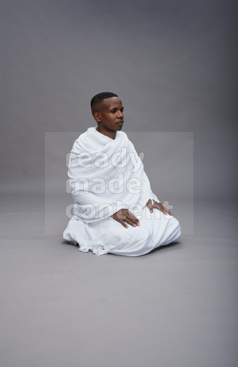A man wearing Ehram sitting on floor praying on gray background