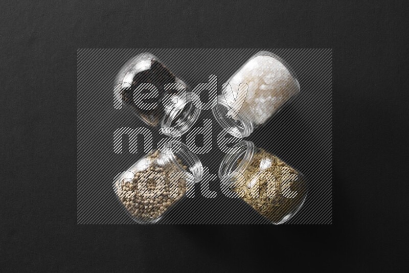 4 glass spice jars full of salt, black peppers, white peppers and cumin on black flooring